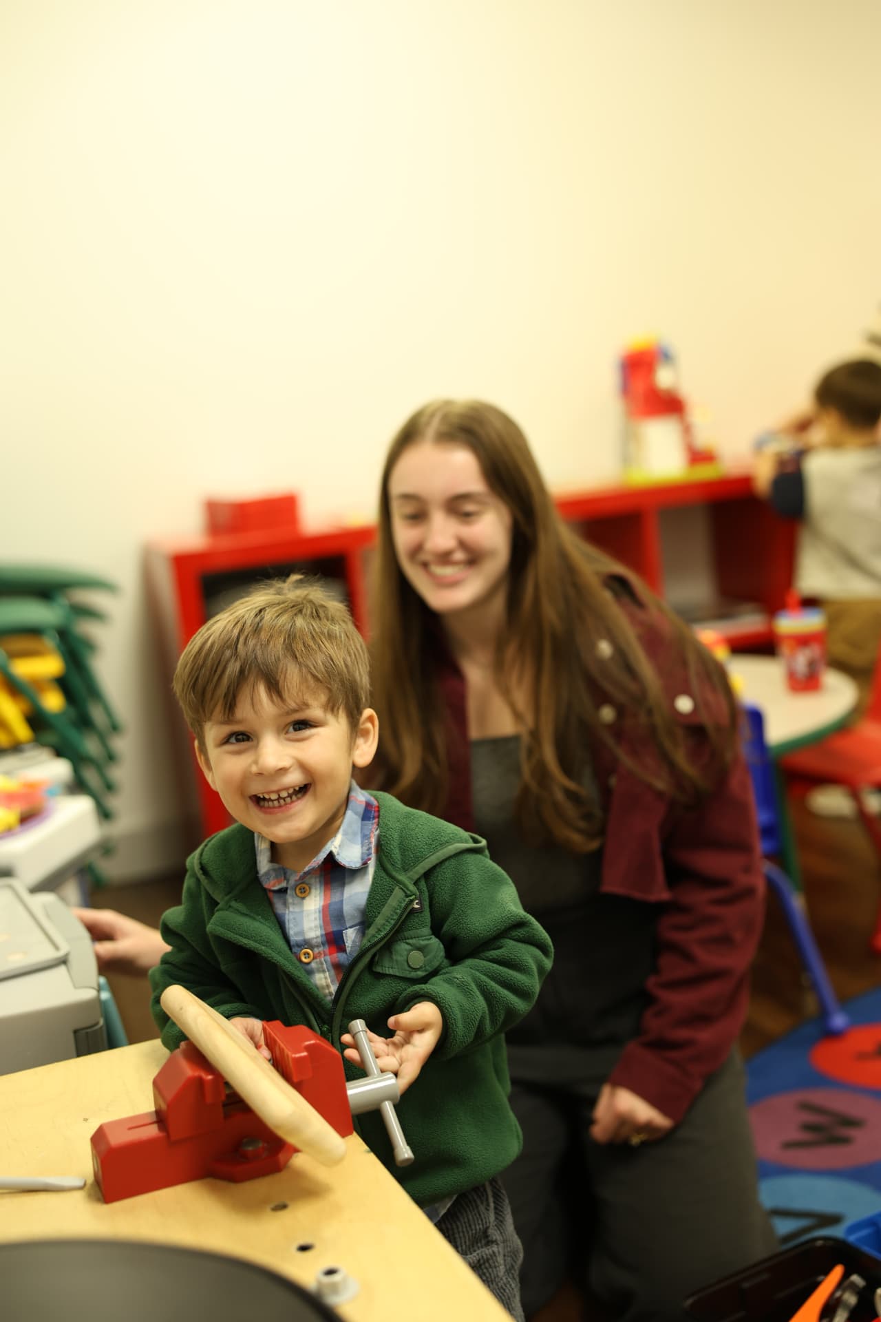 A child smiling while playing at a Salt Kids activity table with a volunteer