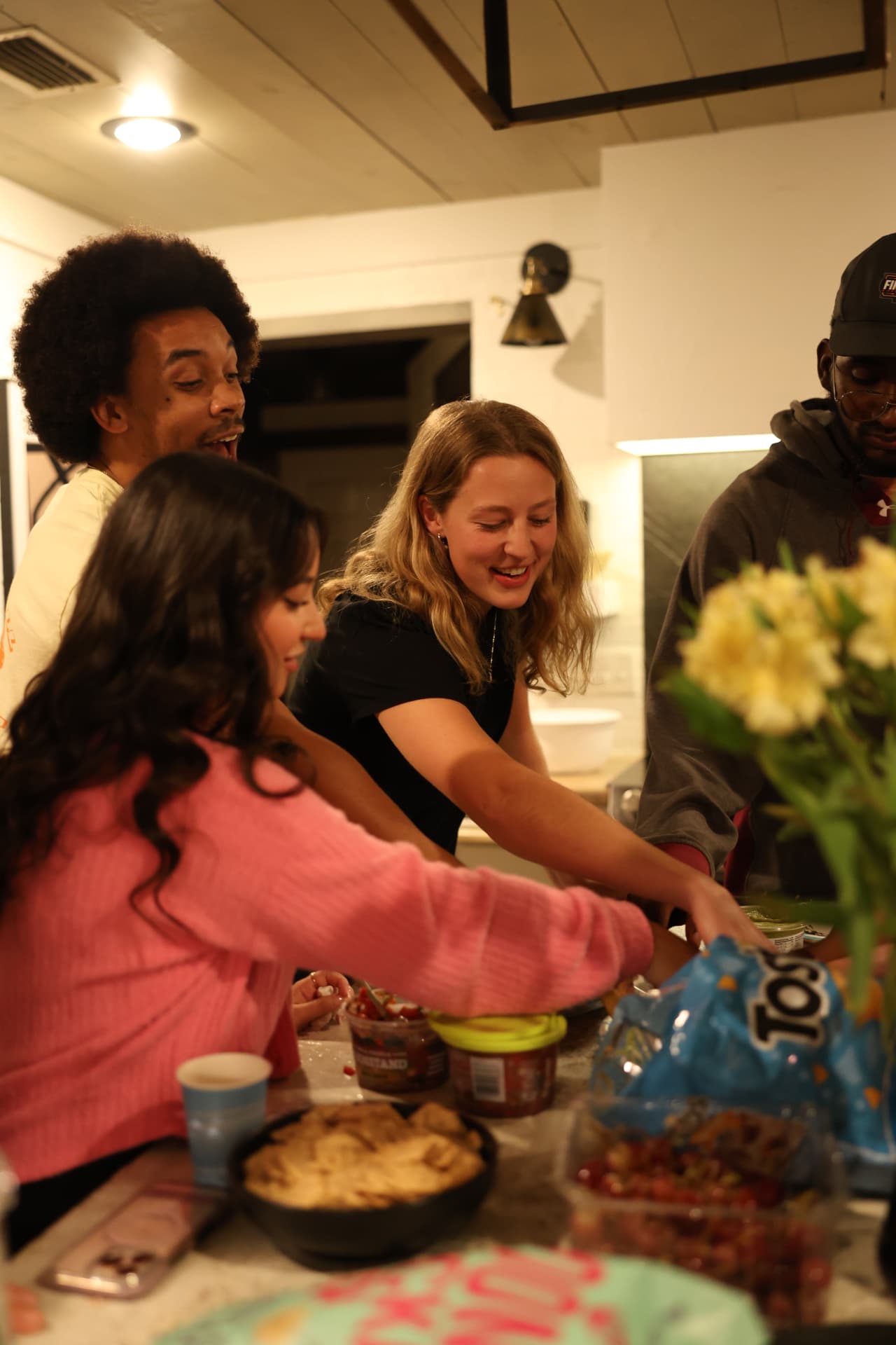 Friends laughing together around a kitchen table with food and drinks