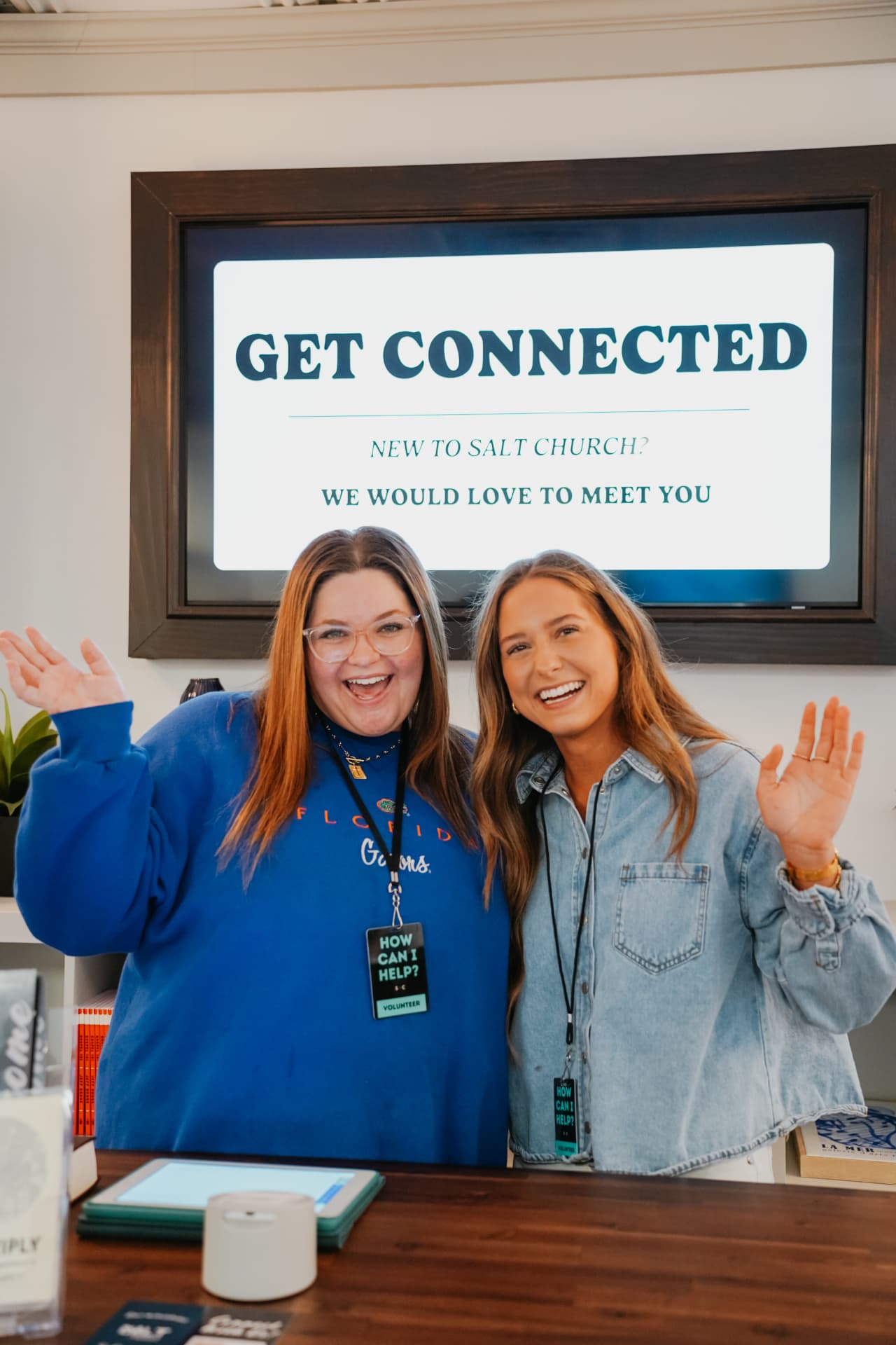 Two smiling Salt Church volunteers waving at the Get Connected welcome desk
