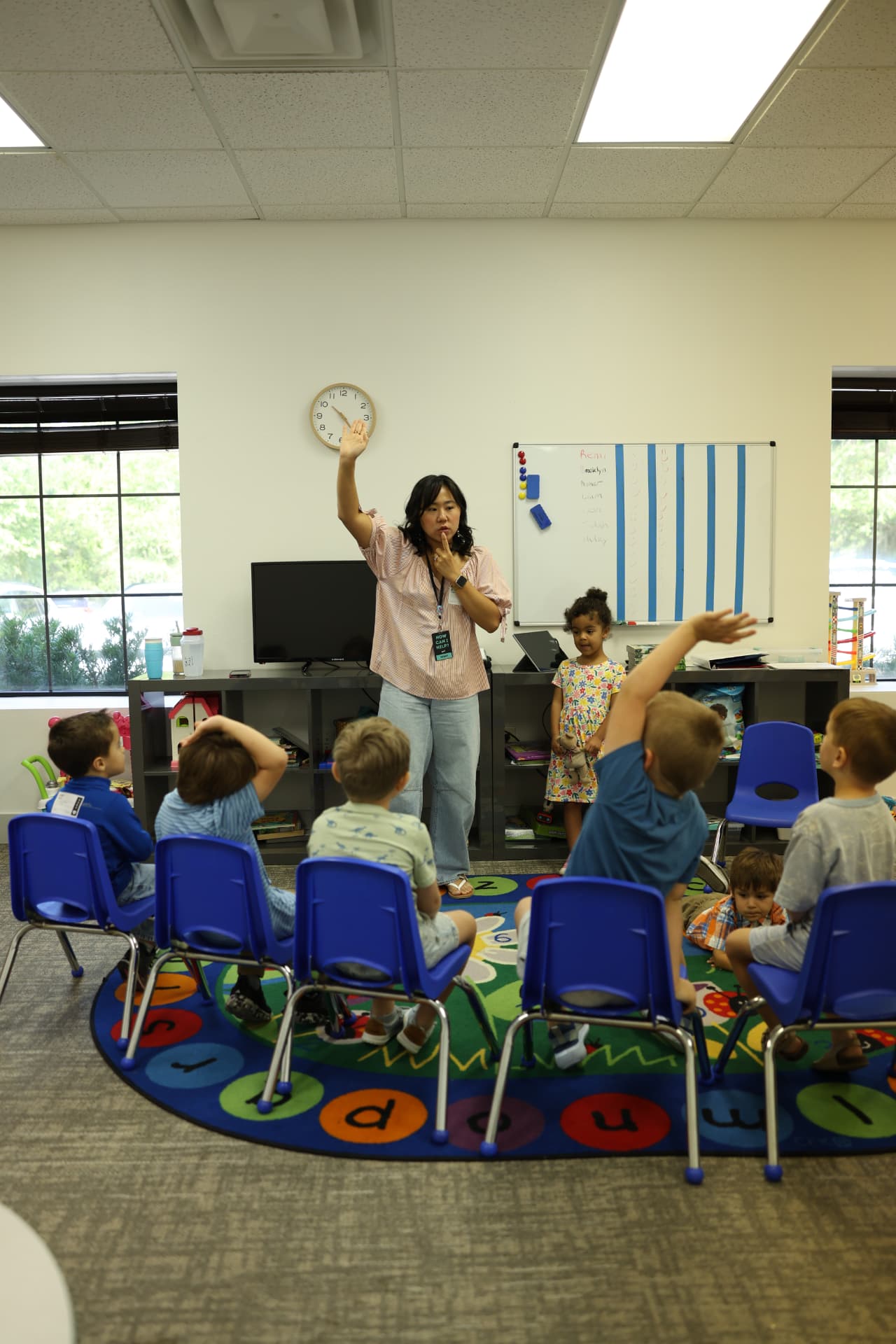 A Salt Kids teacher leading a classroom of children with raised hands