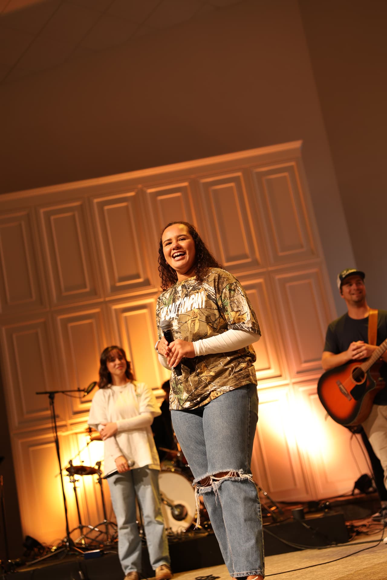 A student leading worship on stage with the band behind her