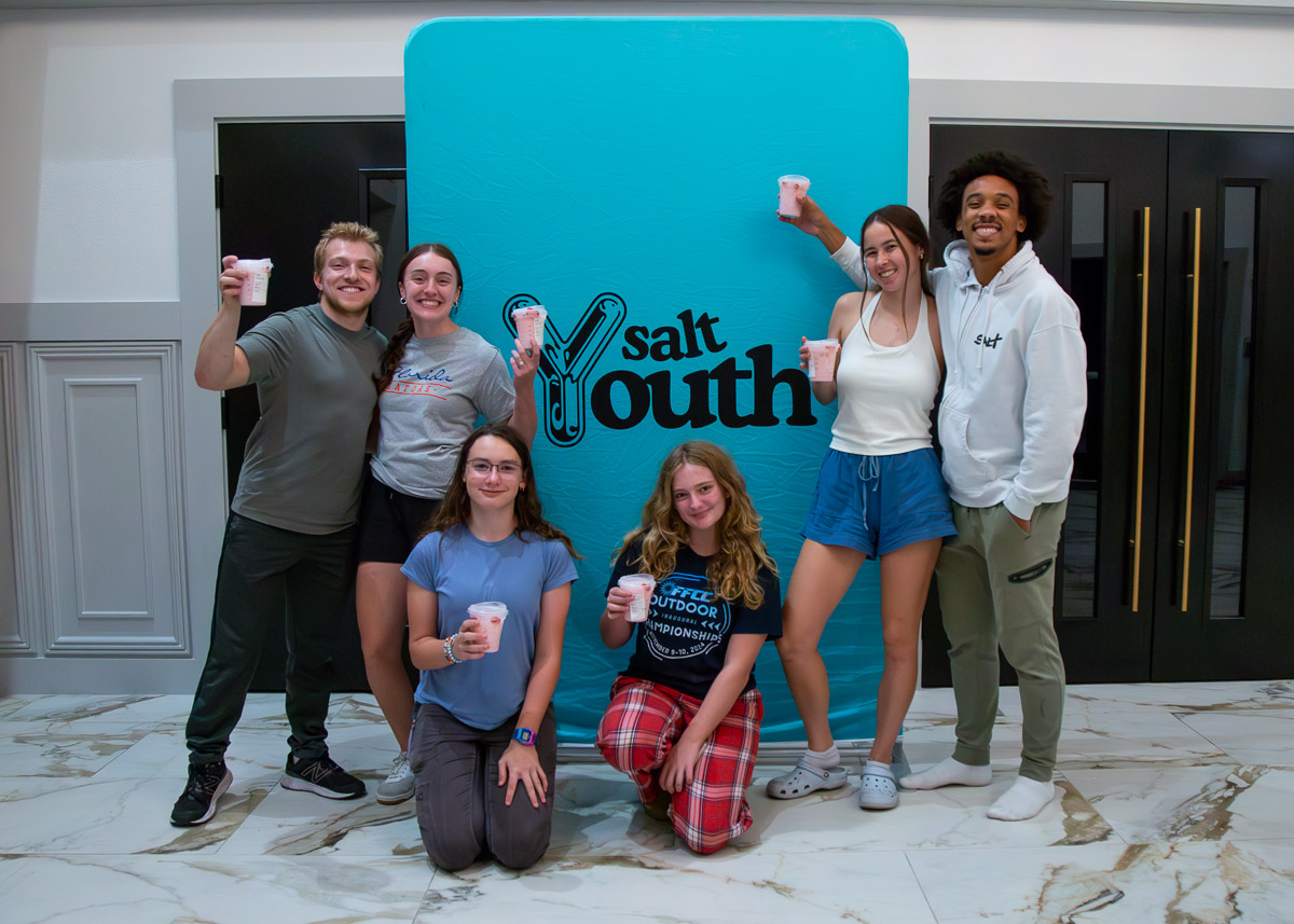 Students celebrating together with Salt Youth milkshakes in front of a branded backdrop