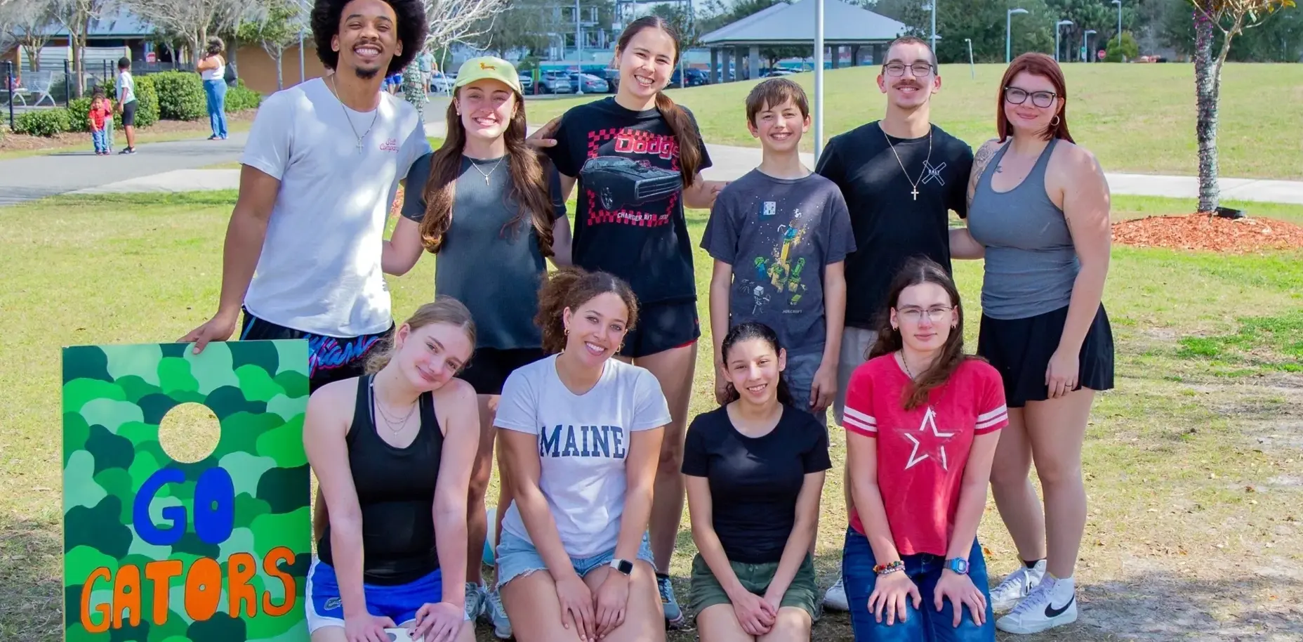 Salt Youth students gathered together outdoors at a park before a cornhole game